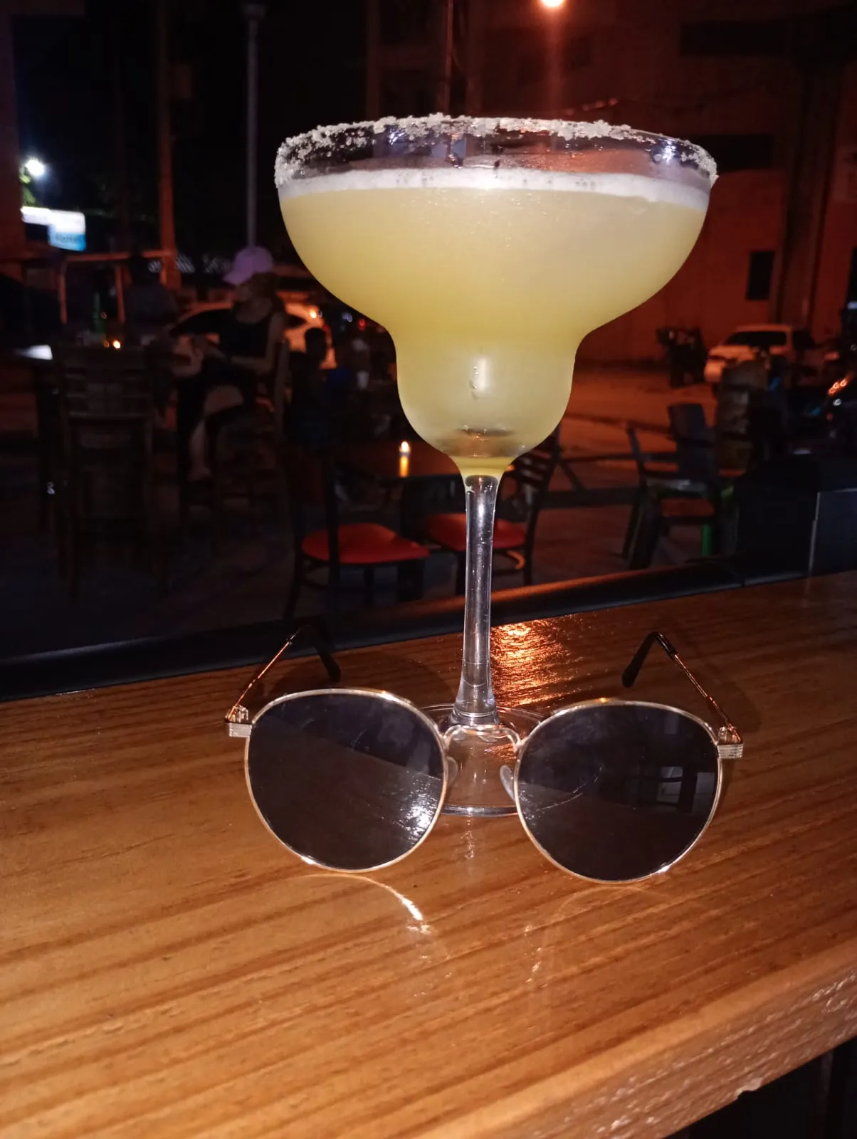A margarita on the wooden bar at night, with the terrace behind it