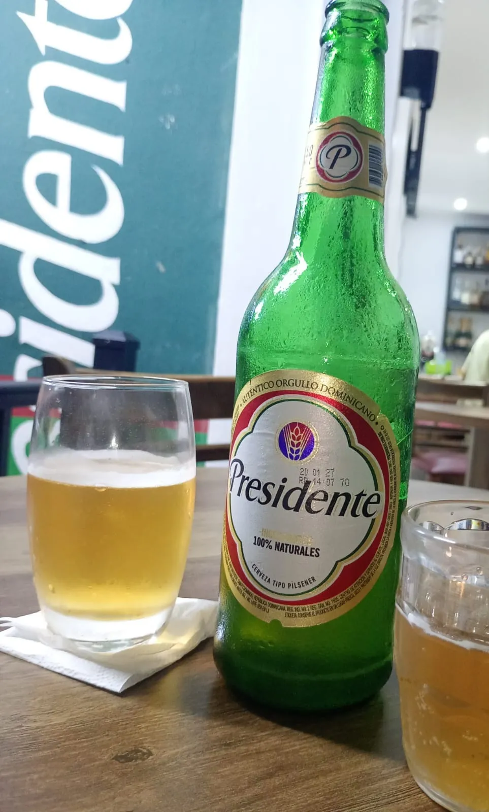 A bottle of Presidente beer with two glasses on a wooden table